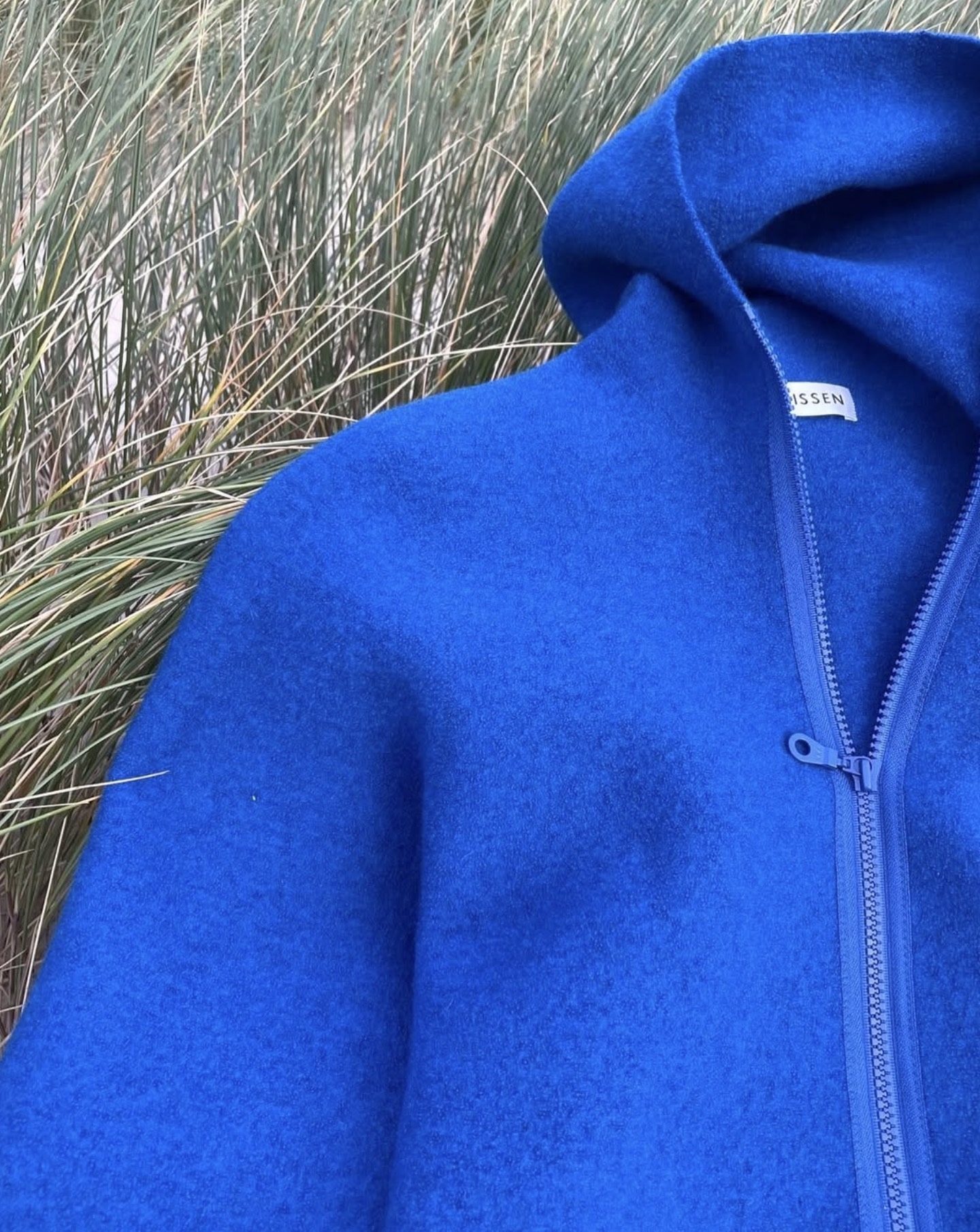 Blaue Walkjacke mit Kapuze im Dünengras